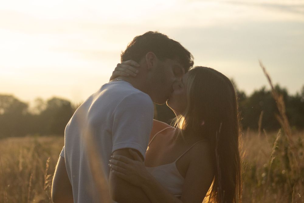 A couple embraces in a golden wheat field at sunset creating a romantic silhouette against the warm sky.