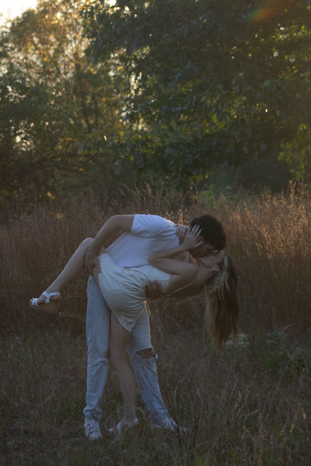 A person in white clothing bends down in a golden field during sunset, creating a silhouetted figure against nature.