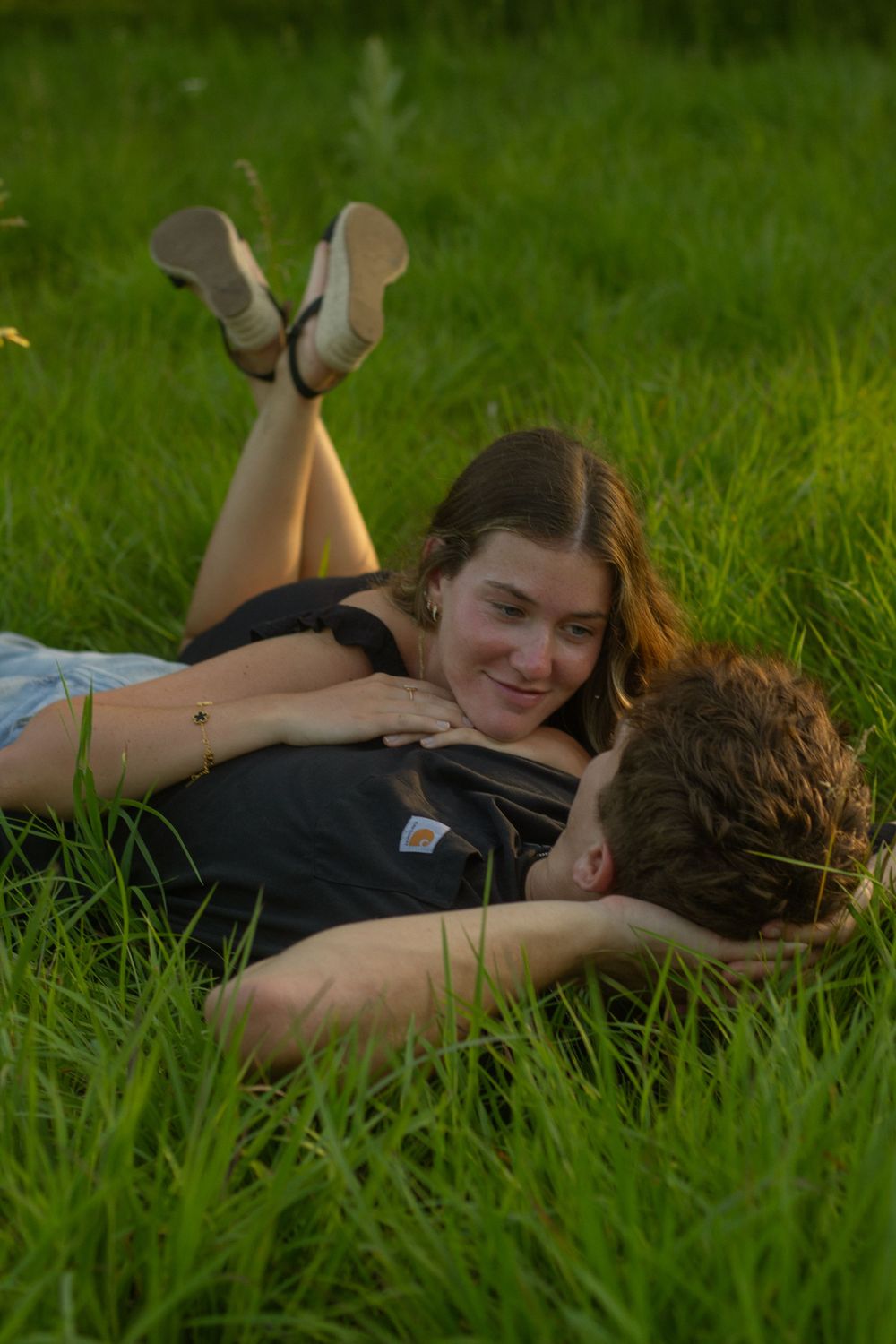 A couple lays together in a grassy field during their couples photos during their summer photos in Flint, Michigan.