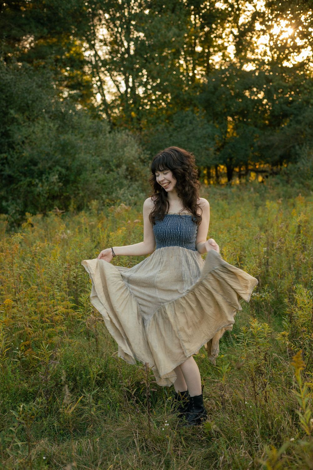 A person in a vintage dress twirls in a golden-lit meadow during sunset during her senior photos at Dominican Meadows, Ann Arbor,  Michigan.