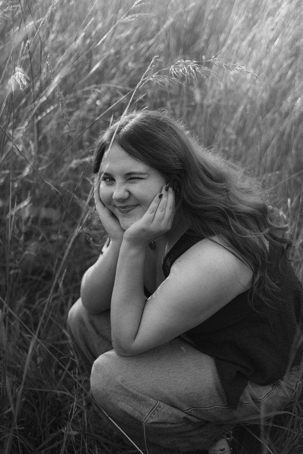 Black and white portraits captured in tall grass showing playful expressions during a senior portrait session in Flushing, Michigan.