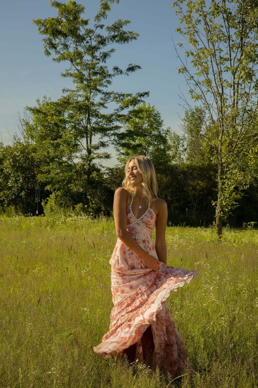 A girl twirls a pink floral dress in a flower field during her senior photos in Davison, Michigan.