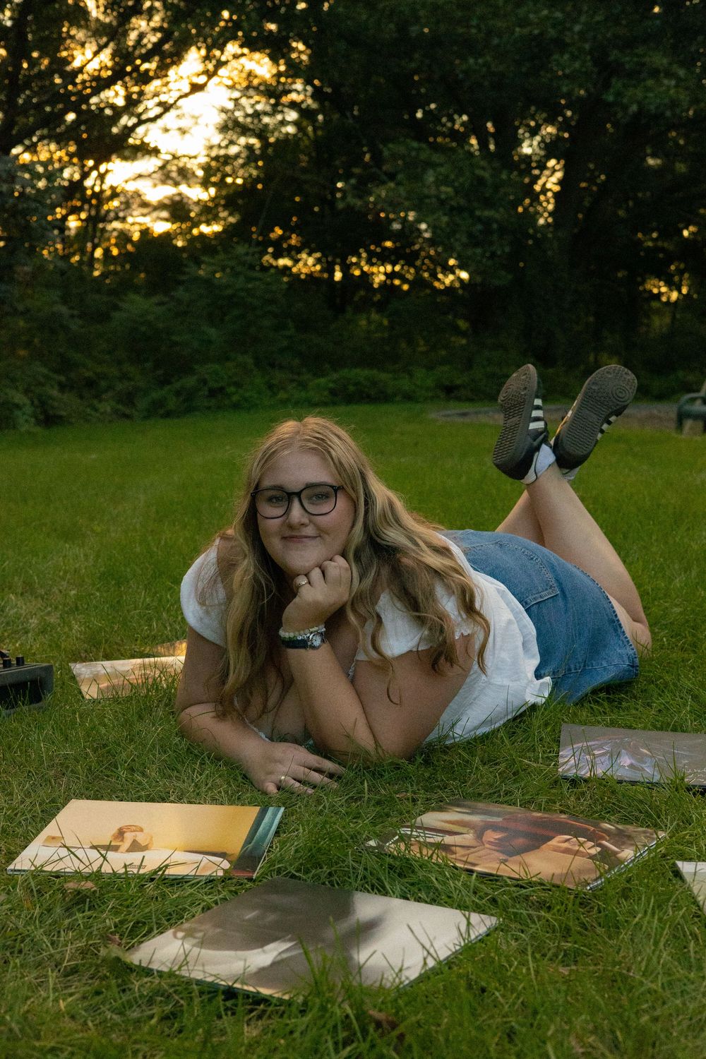 Someone relaxes on a blanket reading books and listening to records in a sunlit summer meadow during a senior photo session in Michigan.