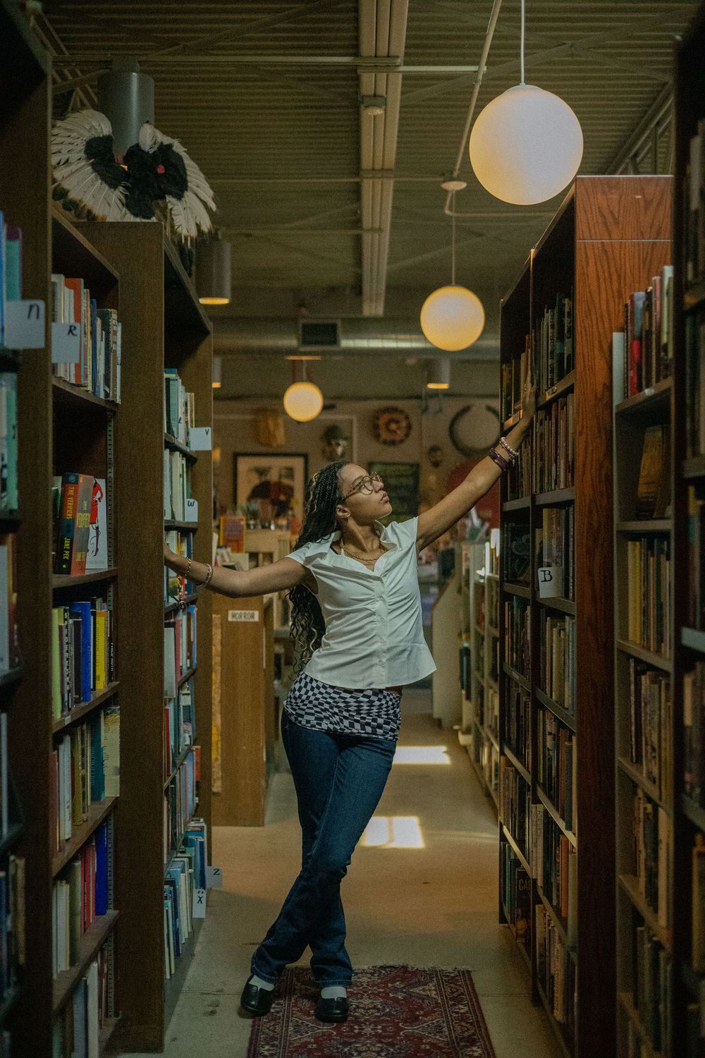 A person in a white top and jeans looks at books at Totem Books in Flint Michigan during her senior photo session.