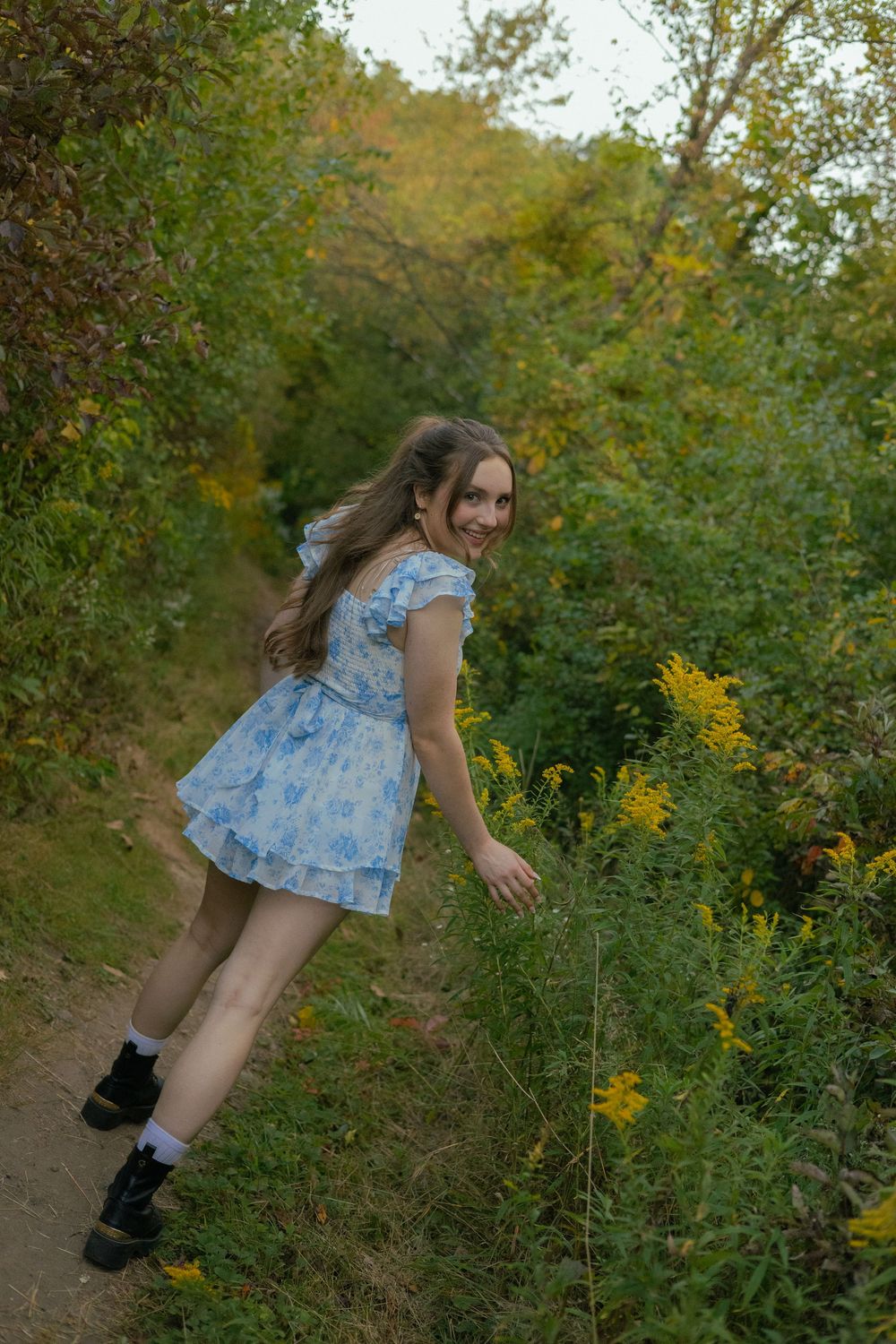 A girl twirls and laughs in a blue floral dress in a flower field during her senior photo session in Ann Arbor, Michigan.