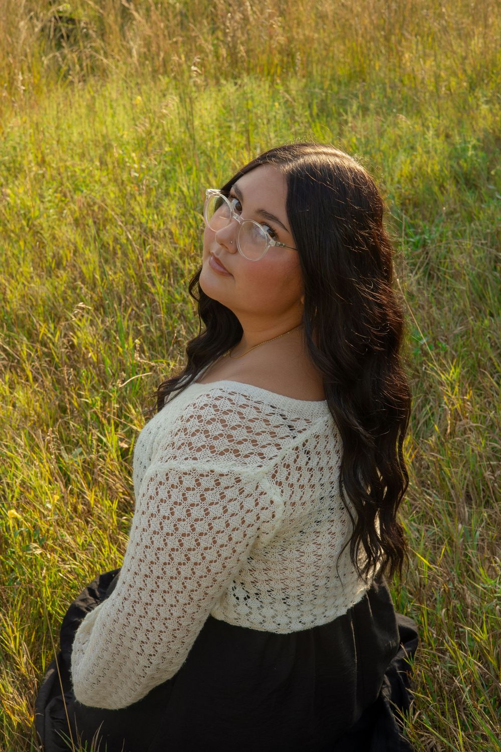 Artistic portraits in golden light showing someone wearing a white crocheted shawl in a meadow during a senior portrait session in Michigan.
