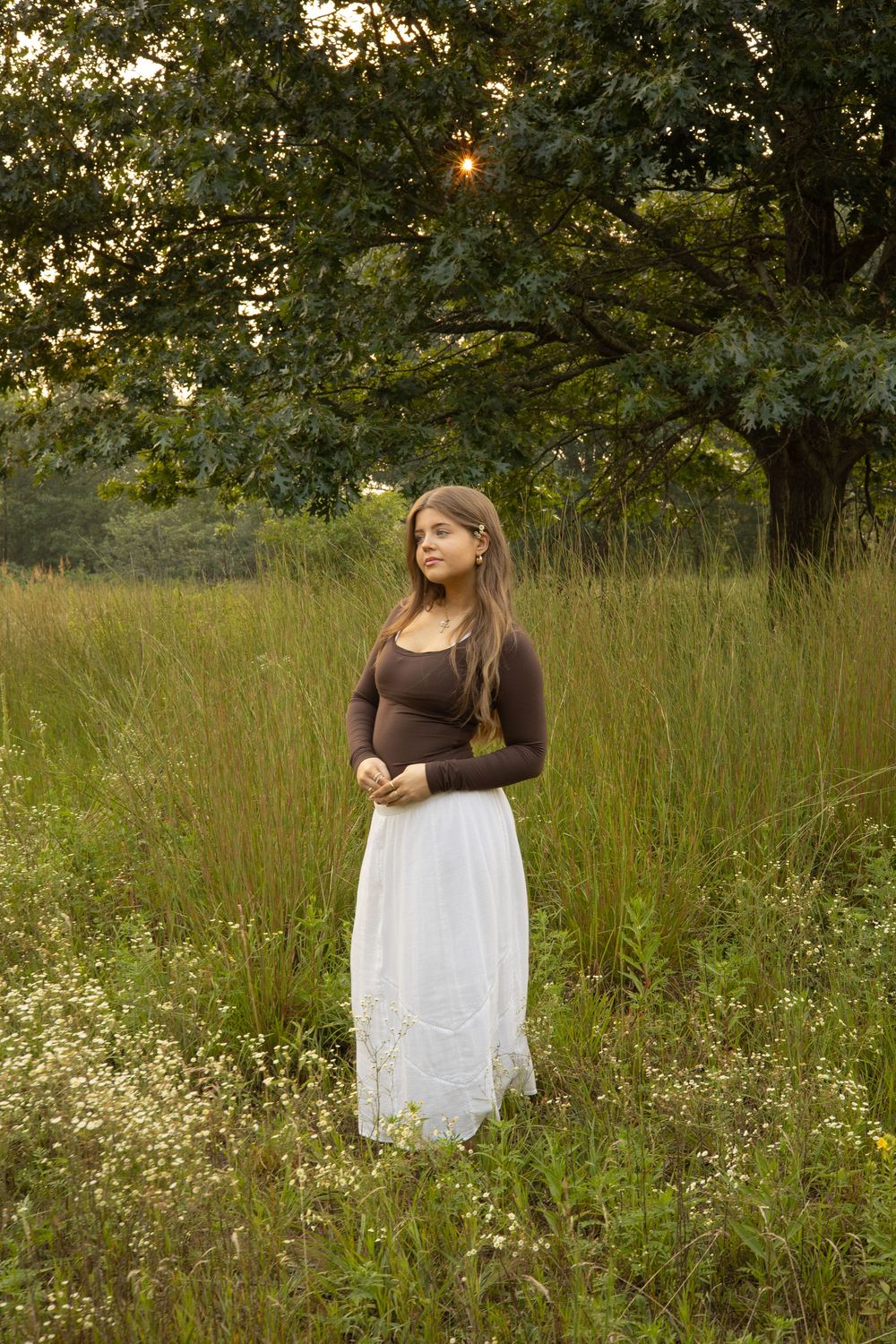 A person in a brown top and white skirt walks through a wildflower meadow at sunset during a photo session for senior portraits in Flushing
