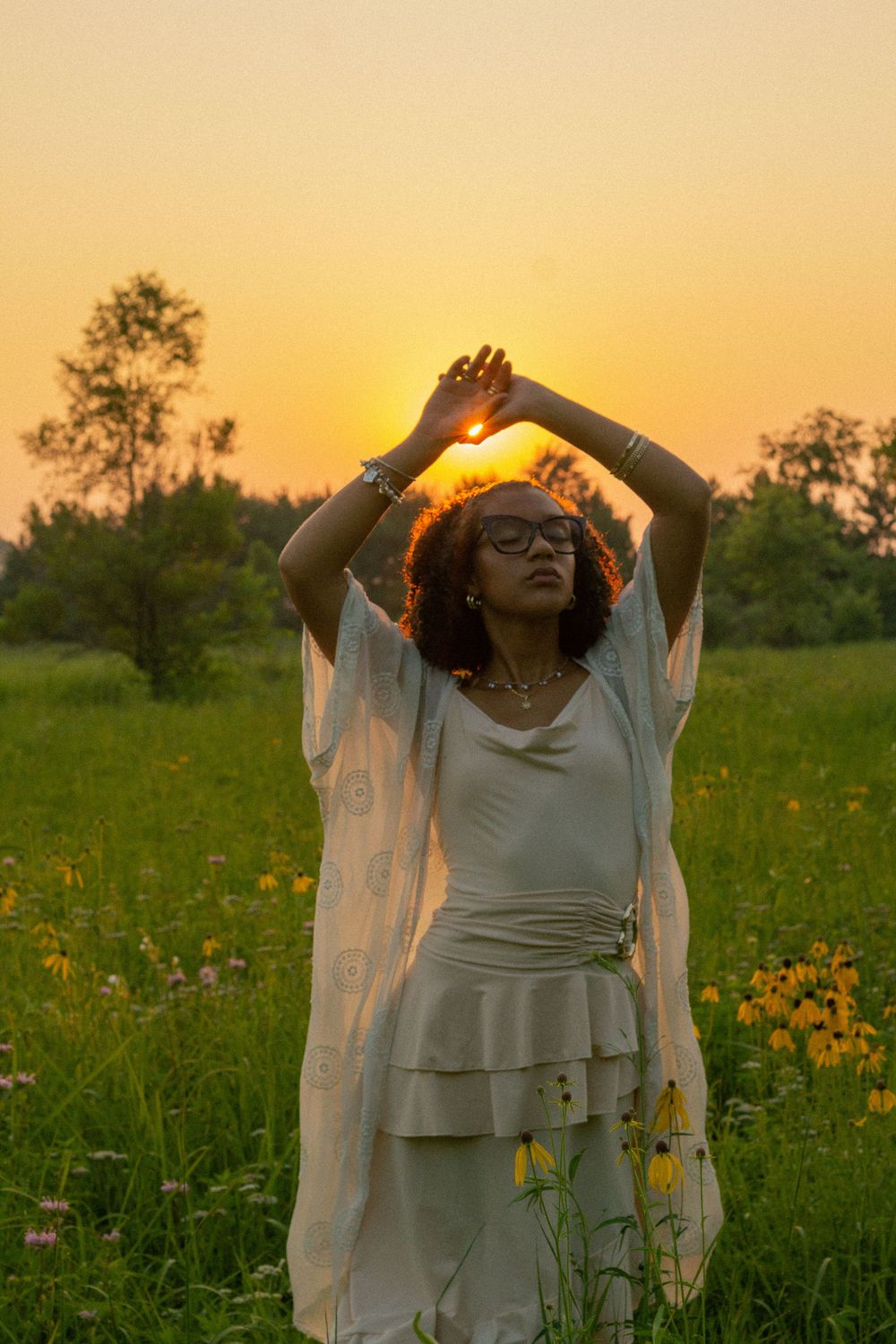 A person in a white flowing dress dances joyfully in a wildflower meadow at golden hour during her senior photo session in Michigan.