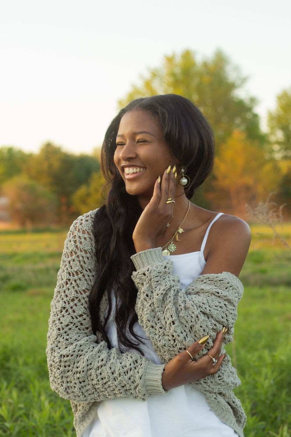 A joyful moment captured in a grassy field at sunset with someone wearing a white dress and chunky knit cardigan.