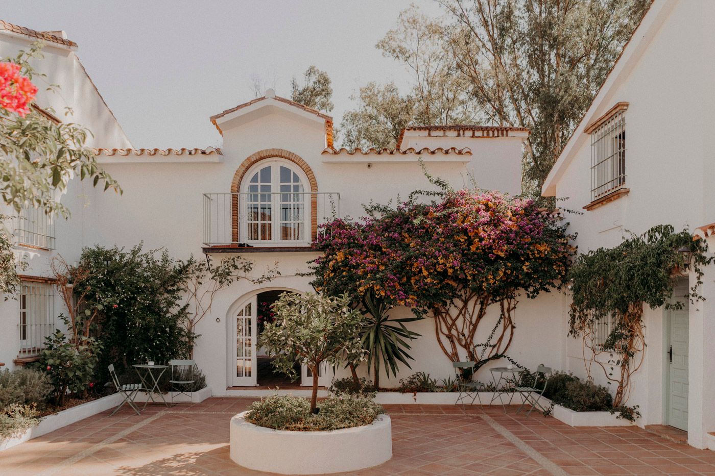 Mediterranean style white stucco home with arched windows and blooming red bougainvillea in a landscaped courtyard.