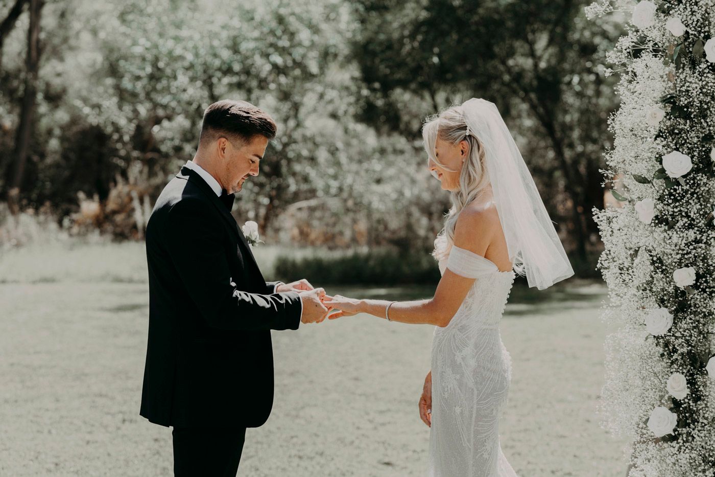 Two people in wedding attire hold hands in a romantic outdoor garden setting during a wedding ceremony.