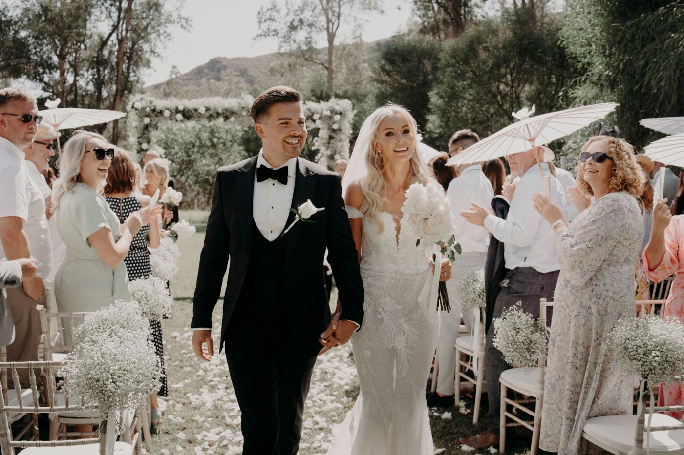 Wedding guests shower celebrating couple with confetti along outdoor garden ceremony aisle during joyful recessional.