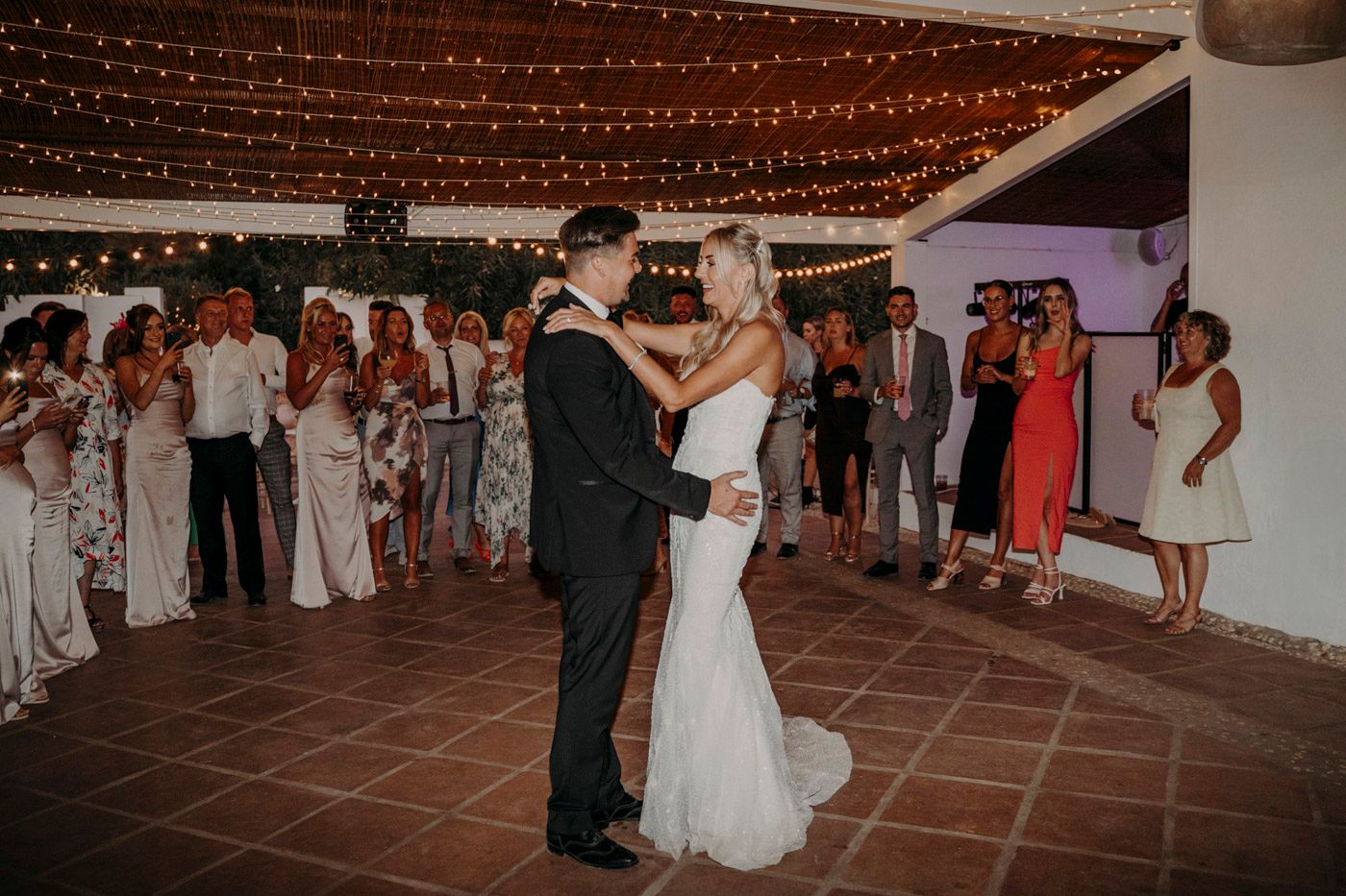 Couple shares their first dance under twinkling string lights at an elegant indoor wedding reception.