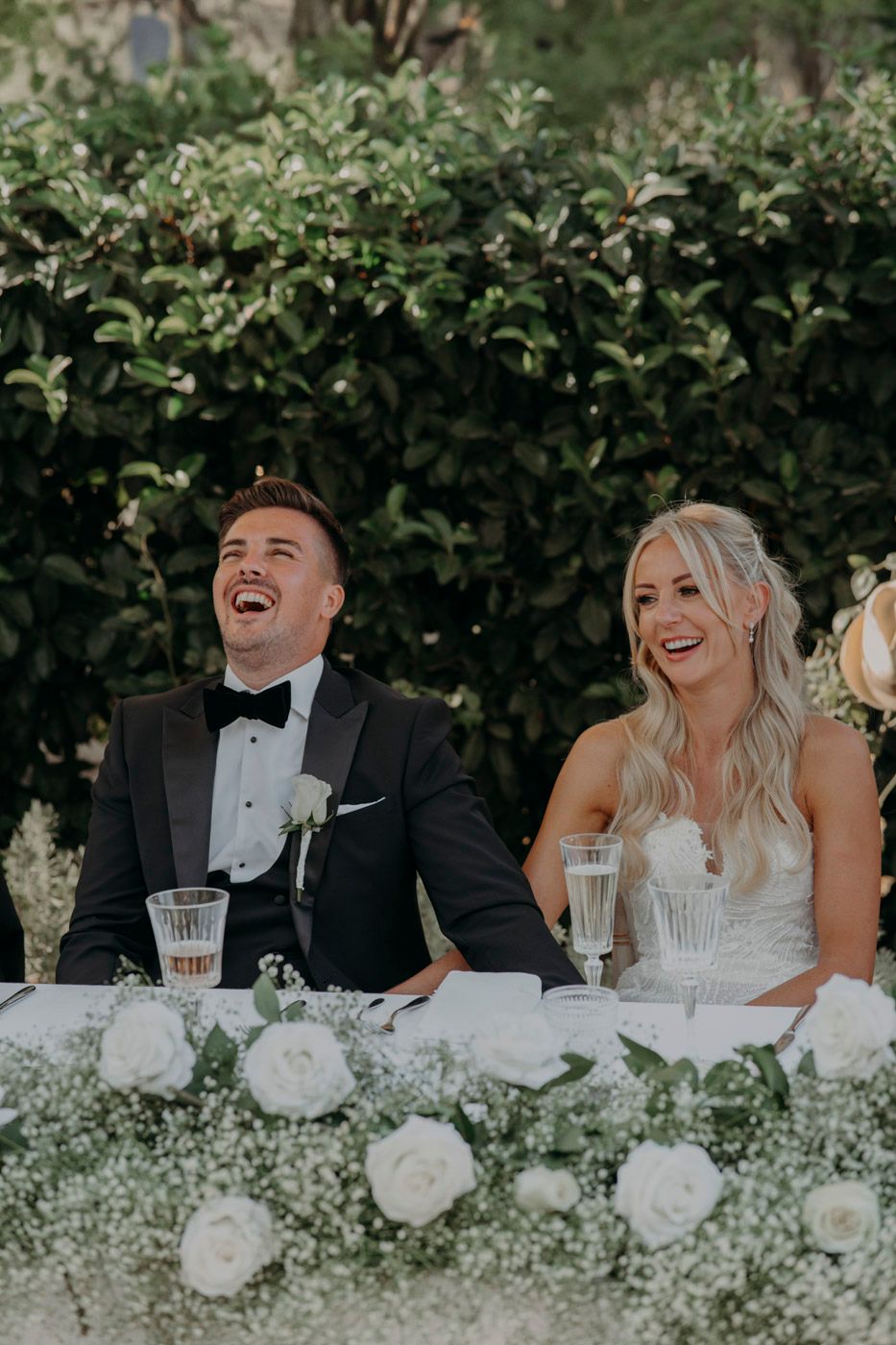 A joyful moment at an elegant wedding reception with white roses and greenery decorating the table setting.