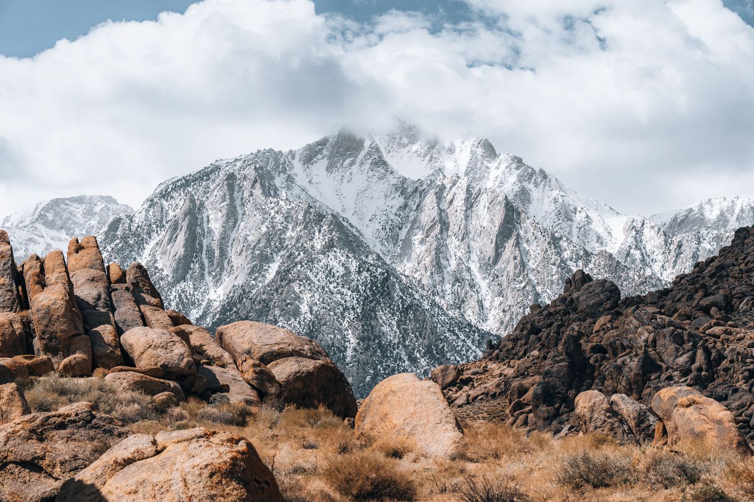 Snow-capped mountain peaks rise above rocky terrain under cloudy skies.