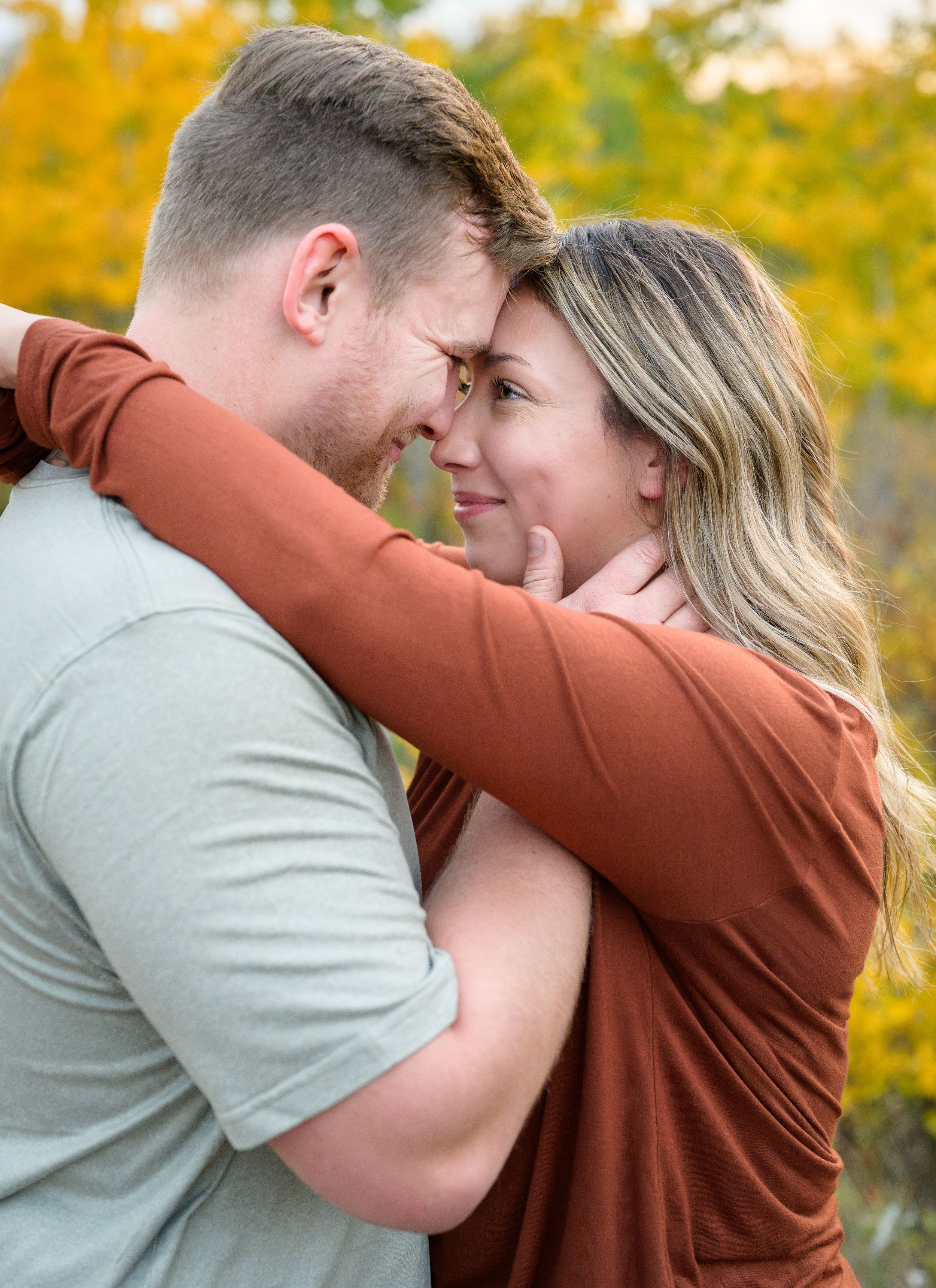 A romantic couple embraces intimately while sharing a tender moment against a backdrop of vibrant yellow fall foliage.