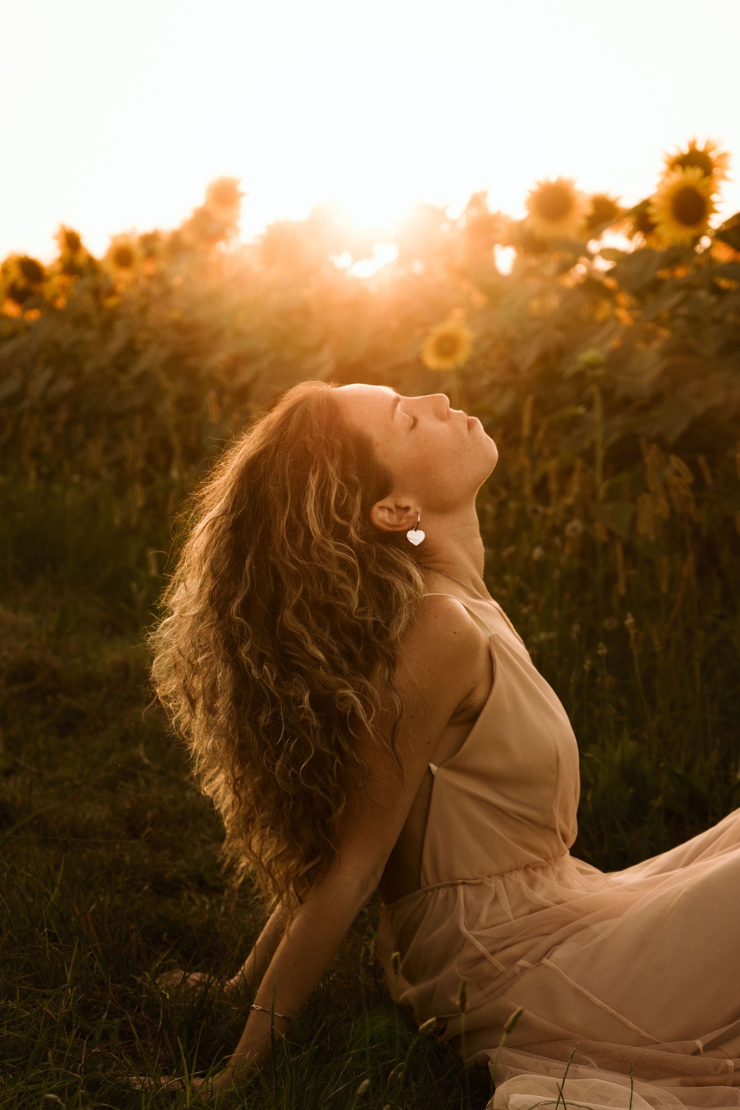 Ritratti sognanti al tramonto in un campo di girasoli in Piemonte con i capelli fluenti e un vestito rosa cipria.
