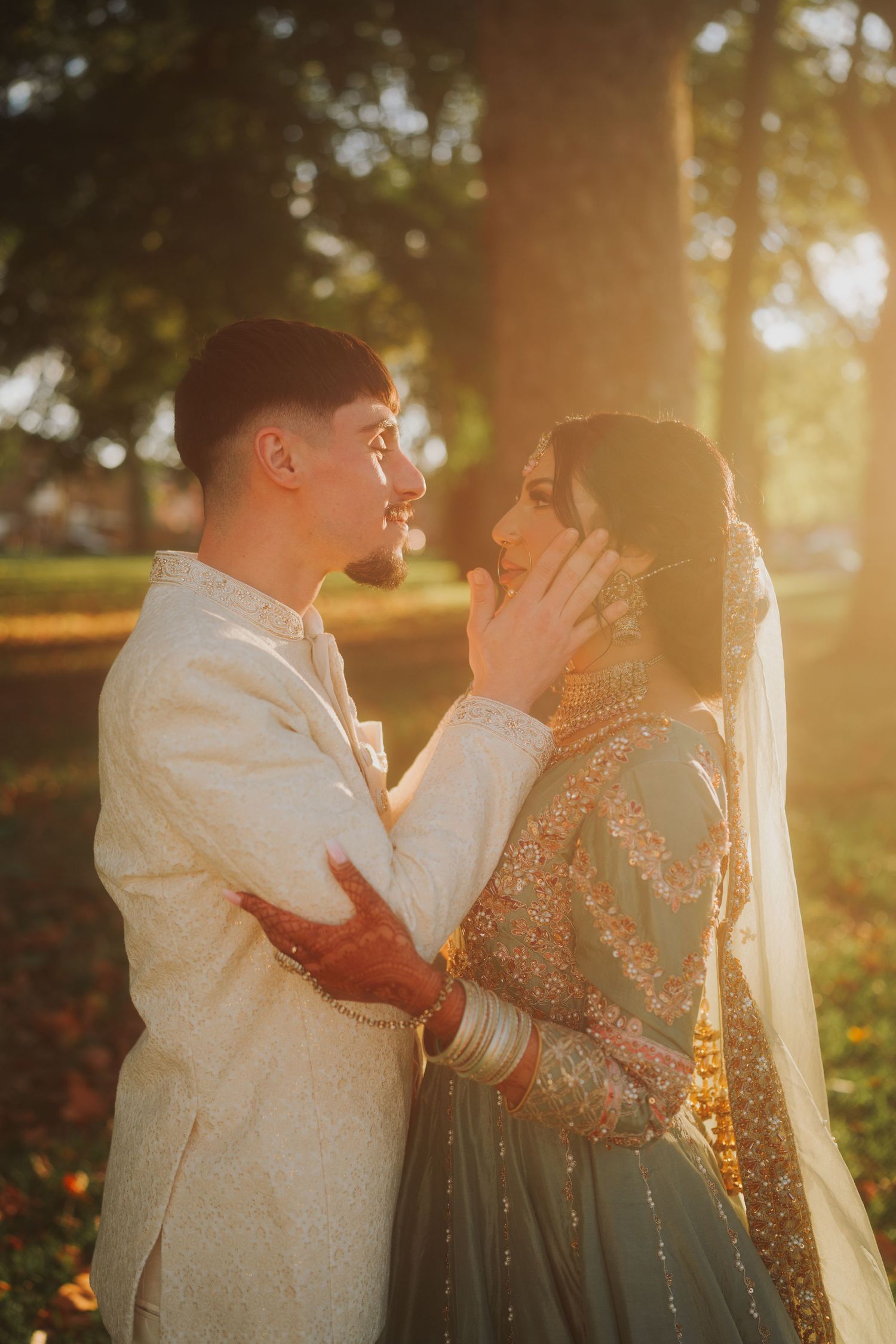 Couple in traditional South Asian wedding attire sharing an intimate moment at sunset in a park.