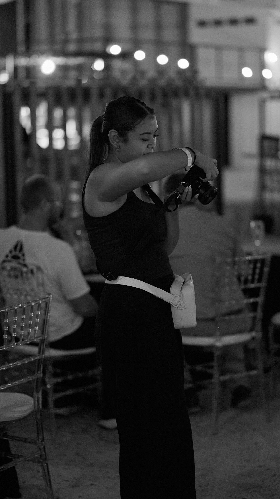 A server in a black uniform with white apron handles payments at a restaurant with blurred lights in the background.