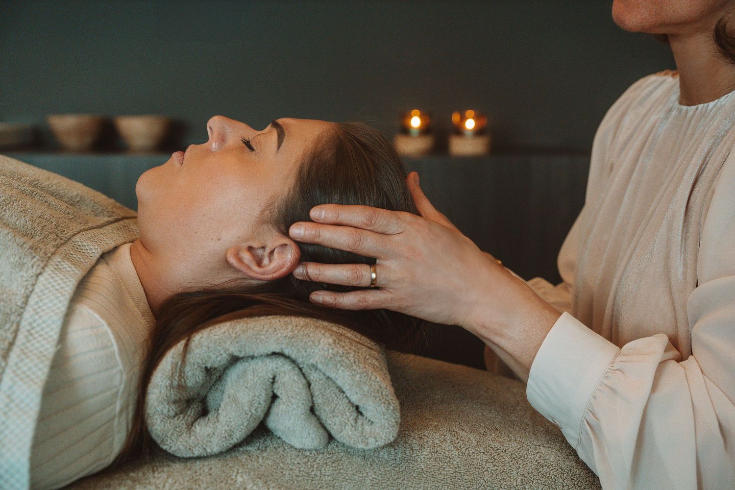 A relaxing head massage session at a spa with candlelit ambiance and towels in the background.