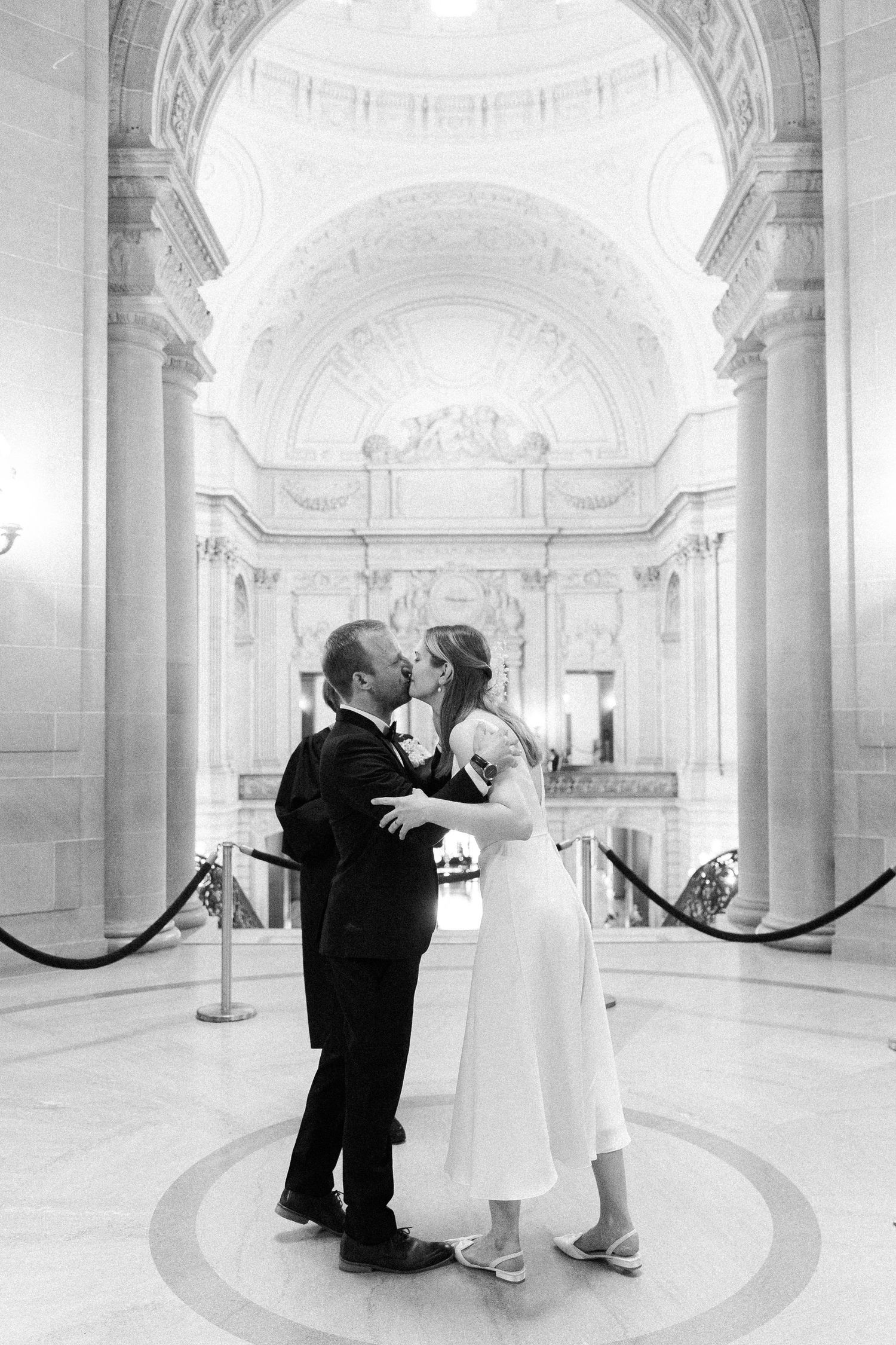 A couple shares a romantic moment in an elegant courthouse hallway with ornate architectural details and vaulted ceilings.