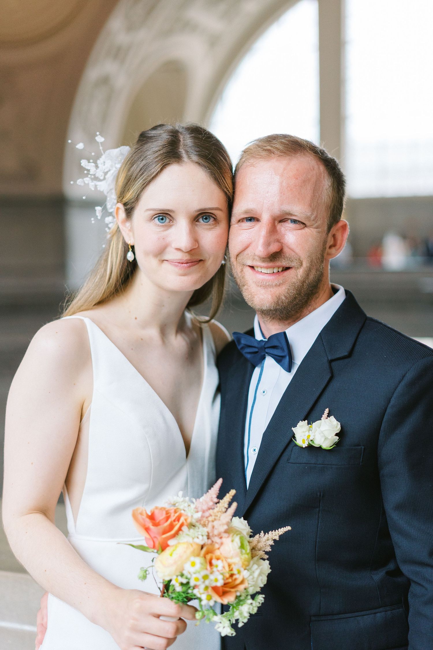 Newlyweds pose together under an archway with a spring floral bouquet.