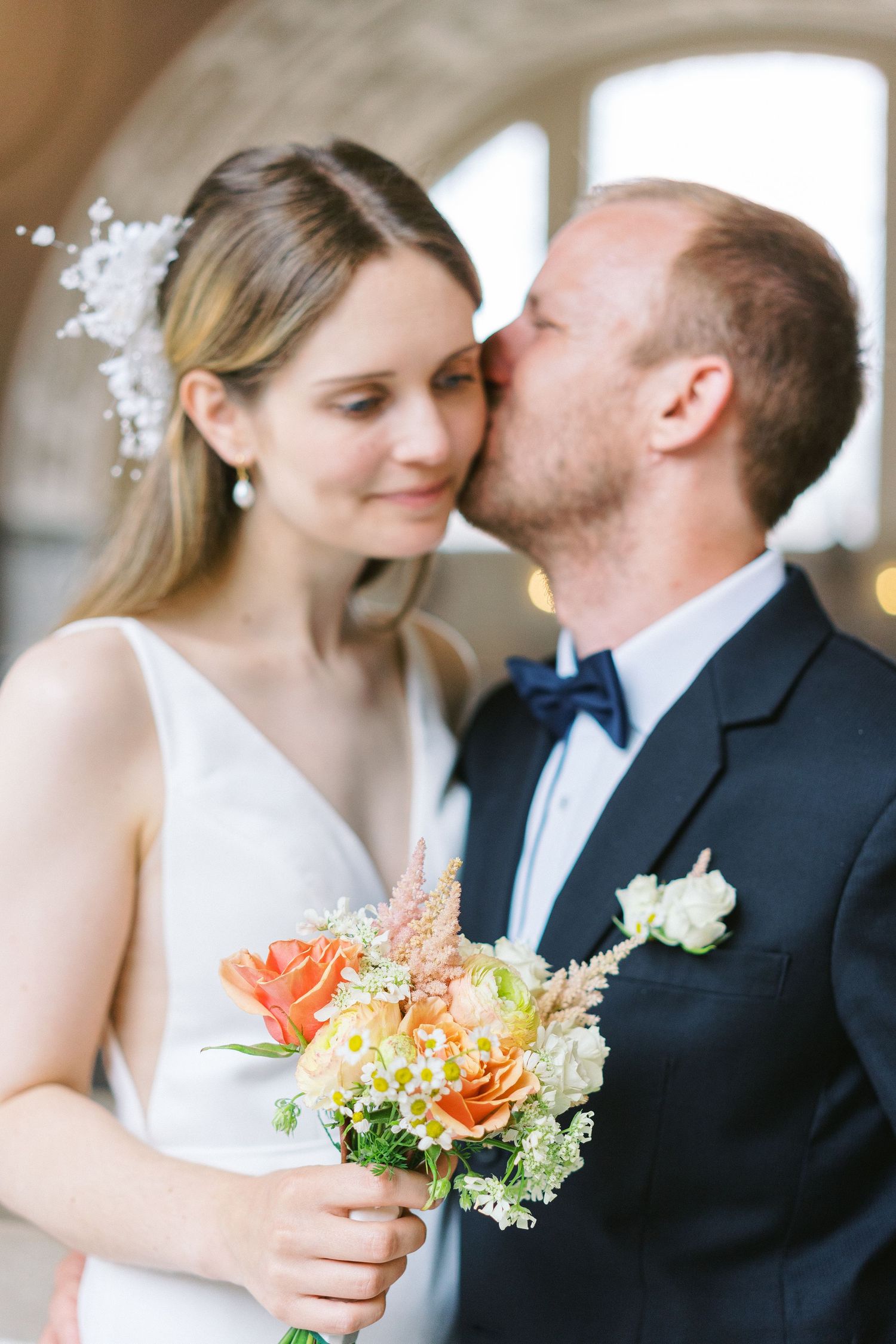 A romantic wedding moment with a couple sharing an intimate pose while holding a coral and white bouquet.