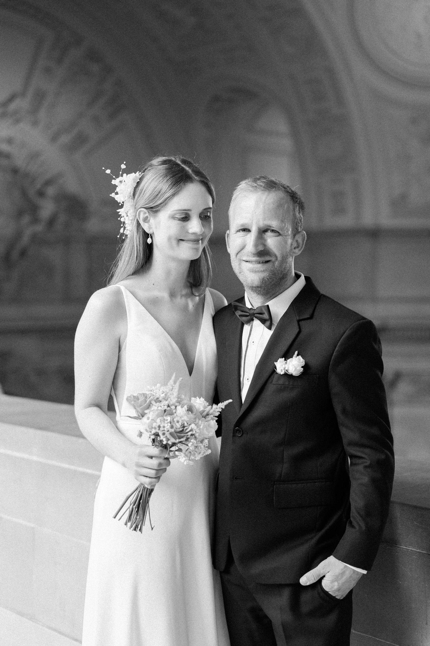 Black and white wedding photograph showing a couple posing together in formal attire with bride holding a floral bouquet.