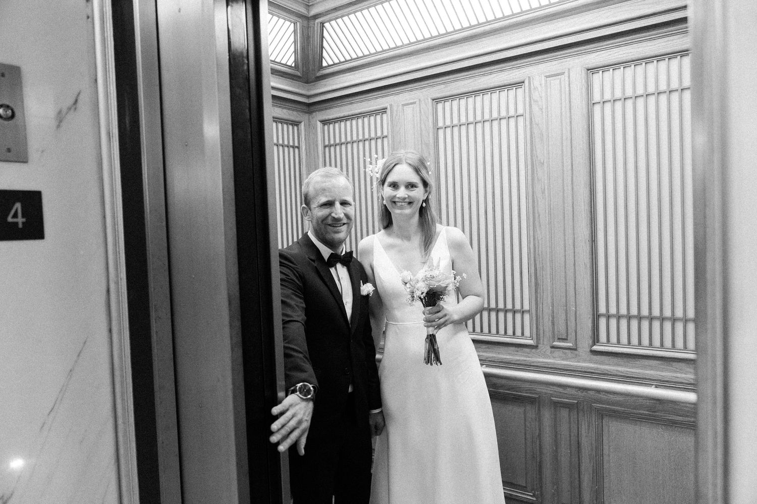 A happy couple shares a moment together in a brightly lit elevator on their wedding day.