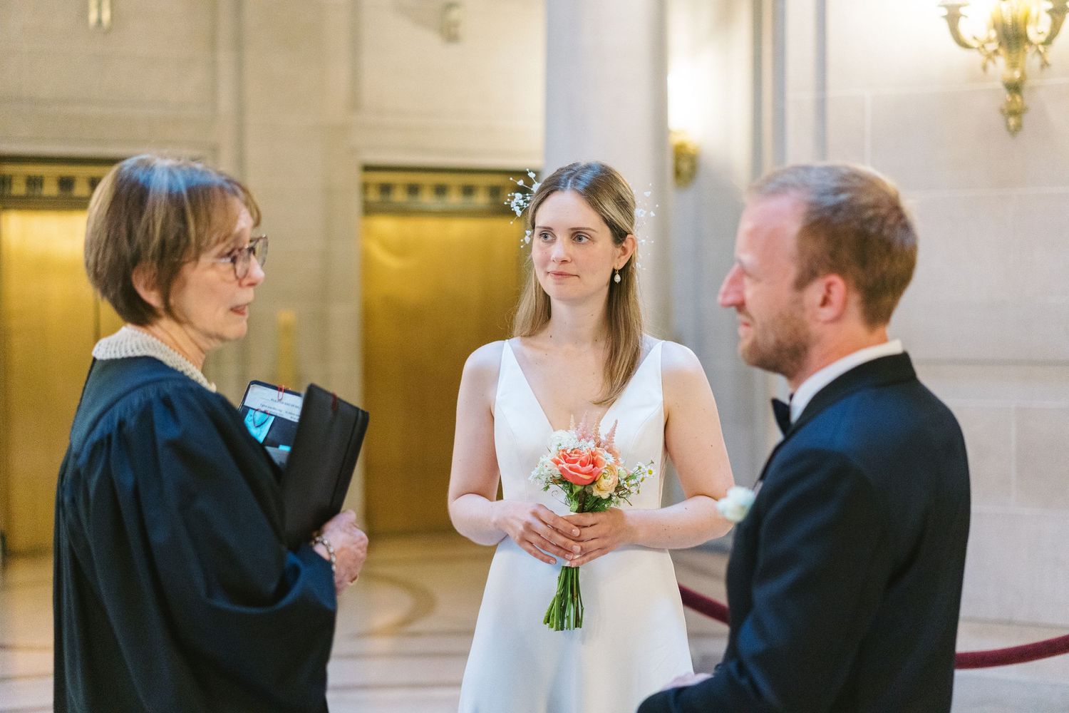 An intimate wedding ceremony takes place indoors with an officiant and couple exchanging vows in an elegant venue.