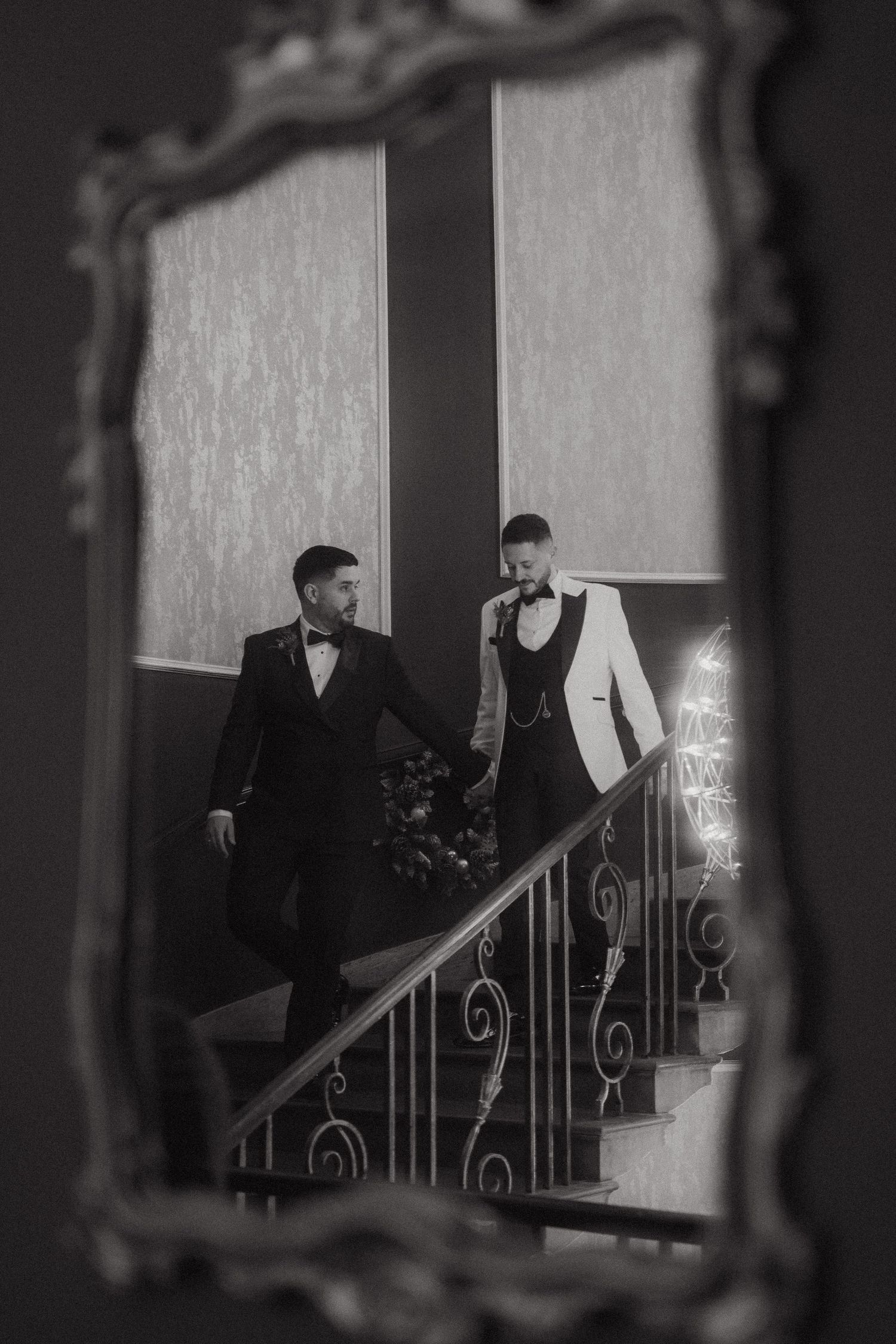 Grooms descend an elegant staircase with ornate railings, framed in a vintage black and white photo.