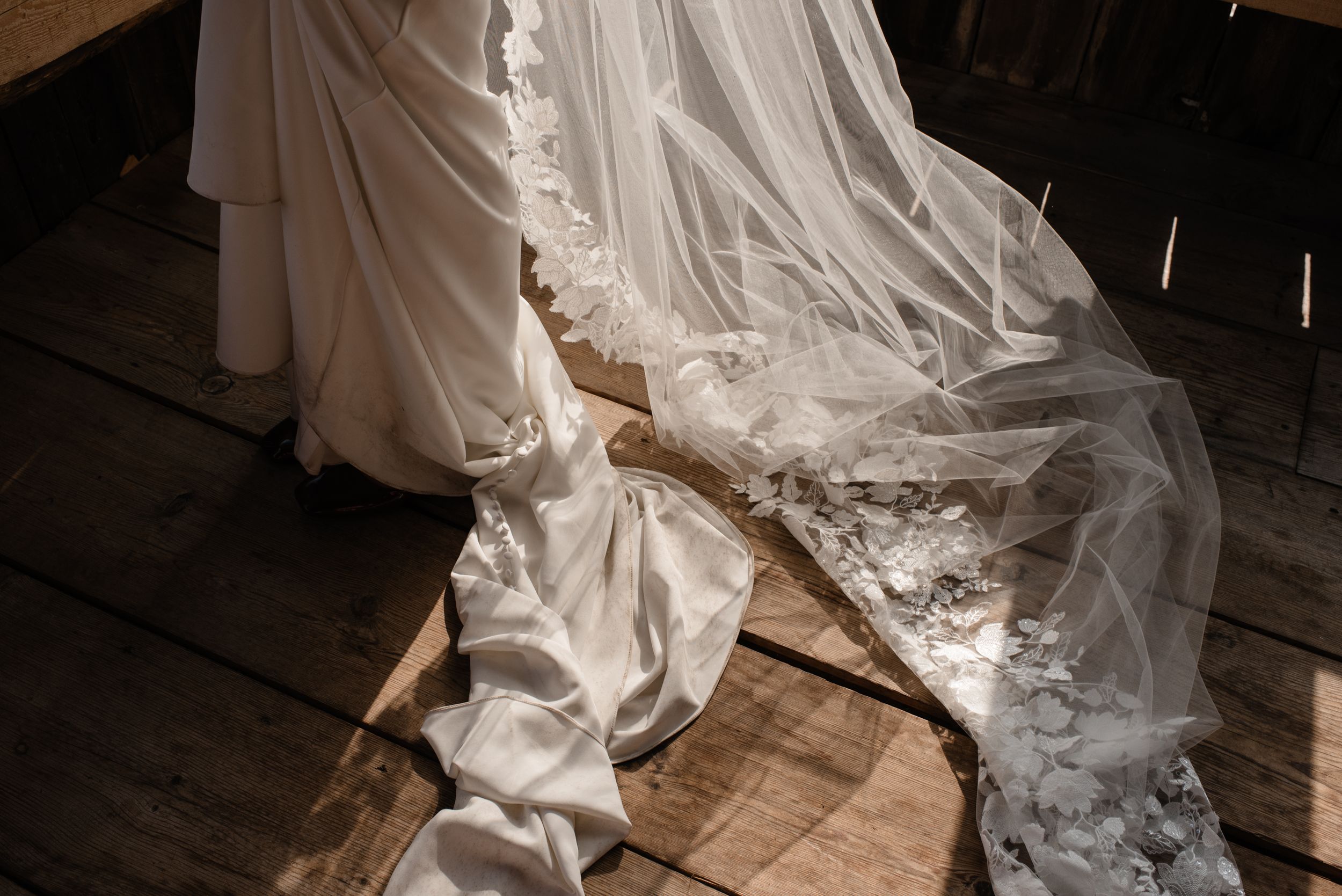 Flowing white wedding dress train and veil trailing elegantly across dark wooden floor boards.
