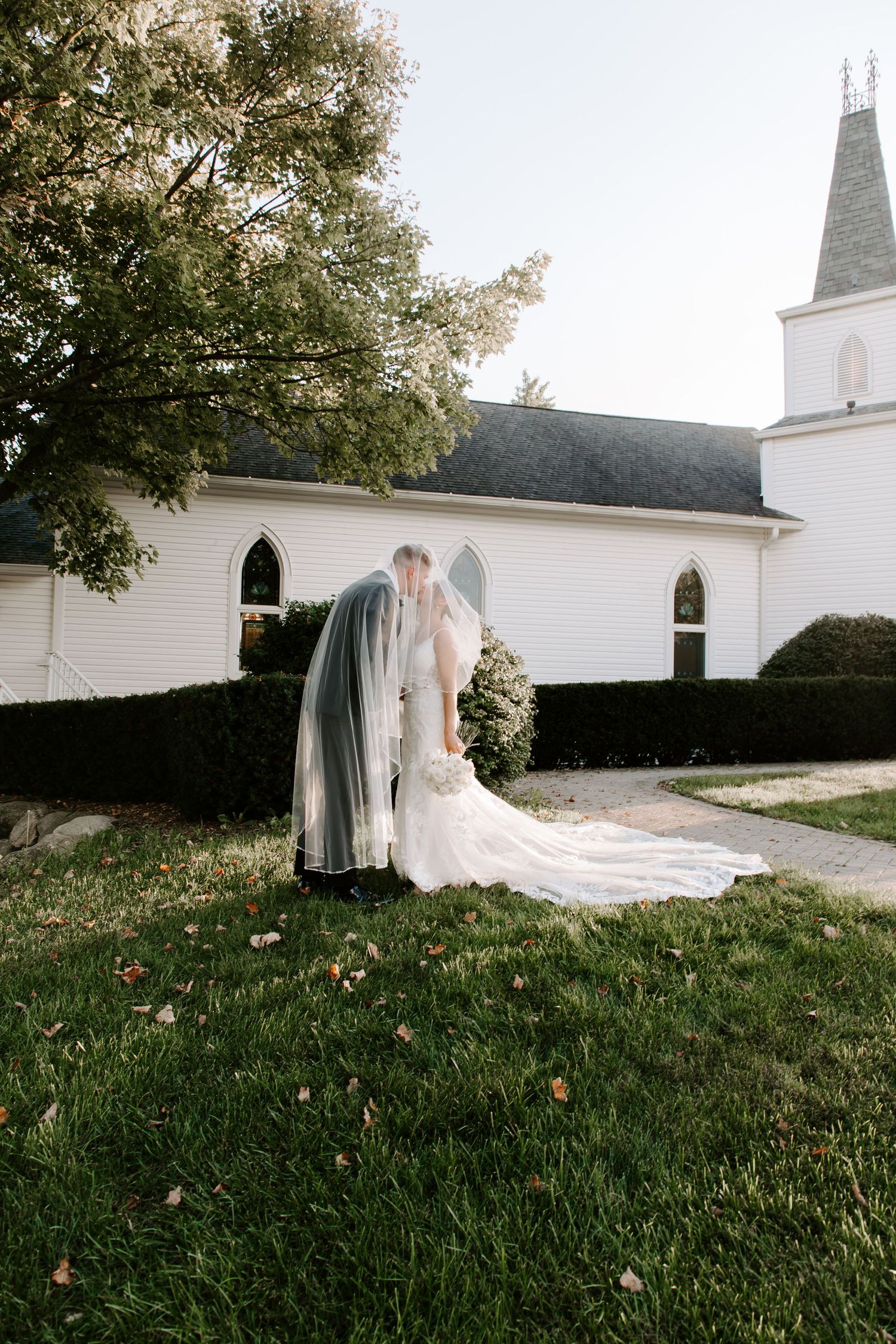 Wedding couple sharing an intimate moment outside a white church with steeple.