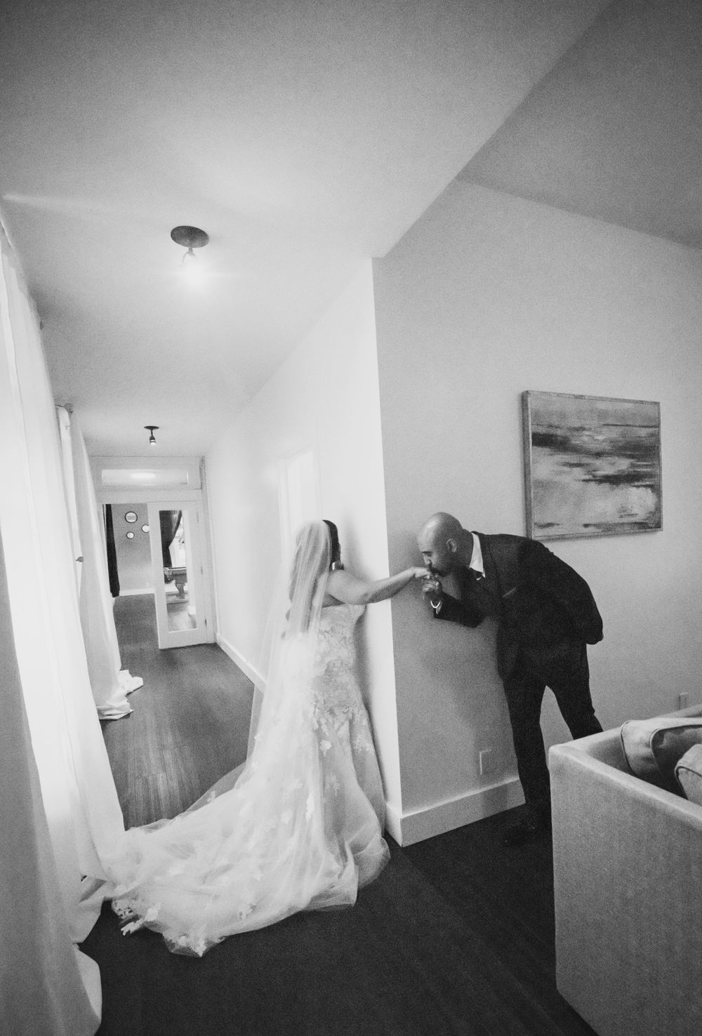 A black and white wedding photo showing a playful moment of peeking around a corner in a hotel hallway.