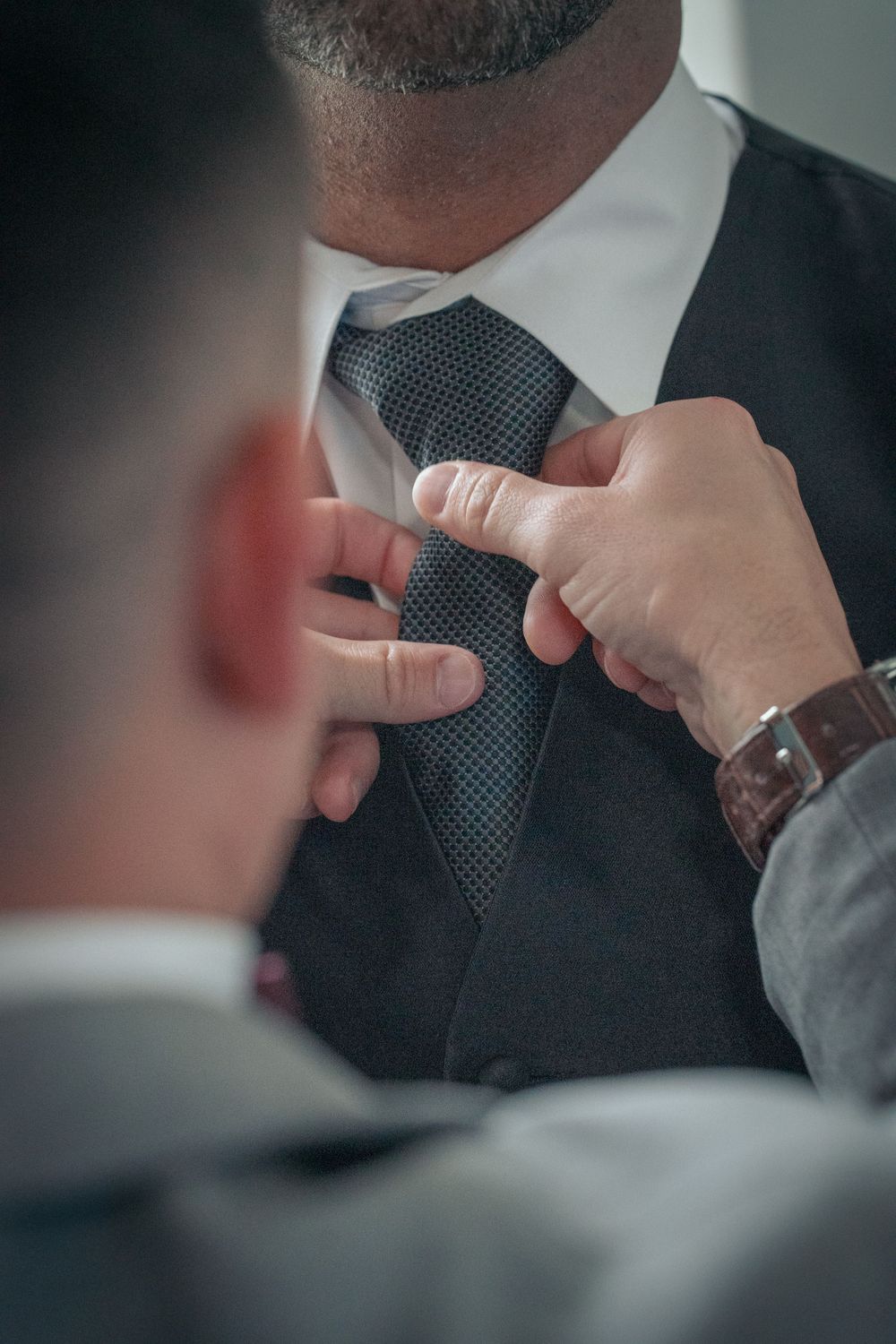 Hands adjust a textured dark gray necktie against a formal vest and white collared shirt.