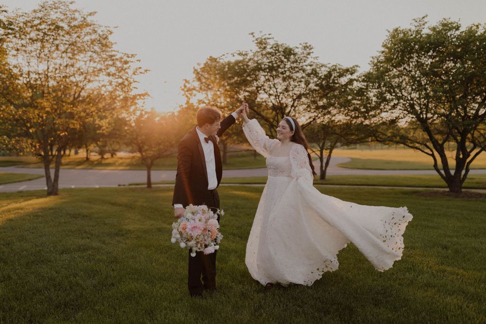 Wedding couple walks through a park at golden hour with trees in the background.