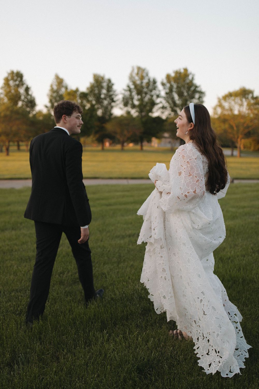 Wedding couple dances and twirls in a grassy field at golden hour.