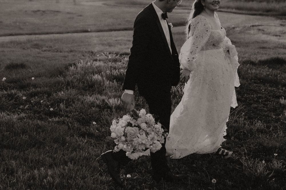 Black and white photo of a couple walking through an outdoor field at their wedding.