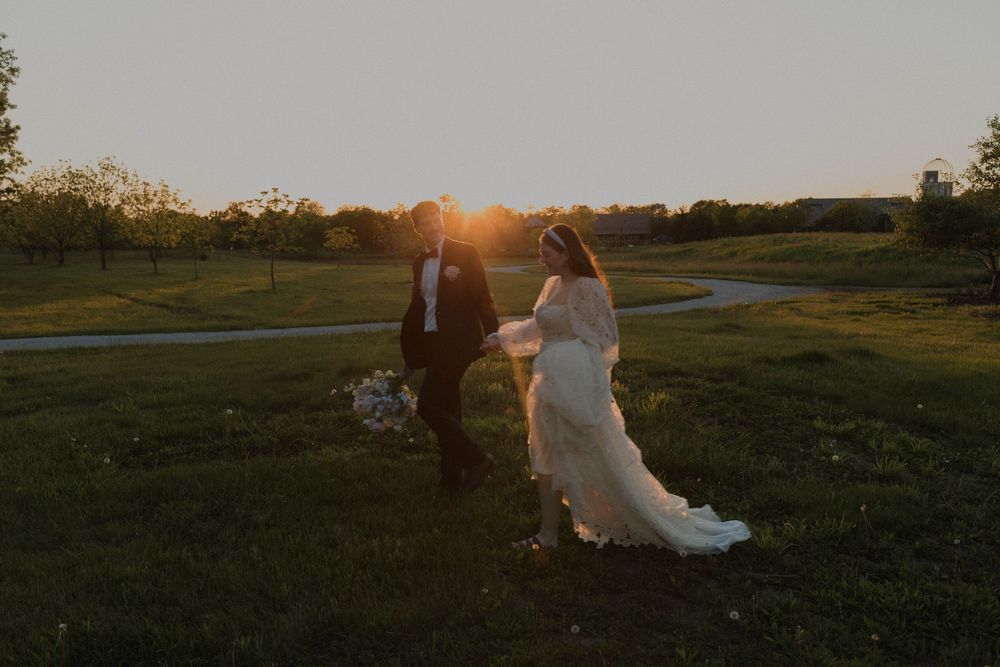 Silhouetted couple walks across a sunset-lit meadow during their wedding photoshoot.