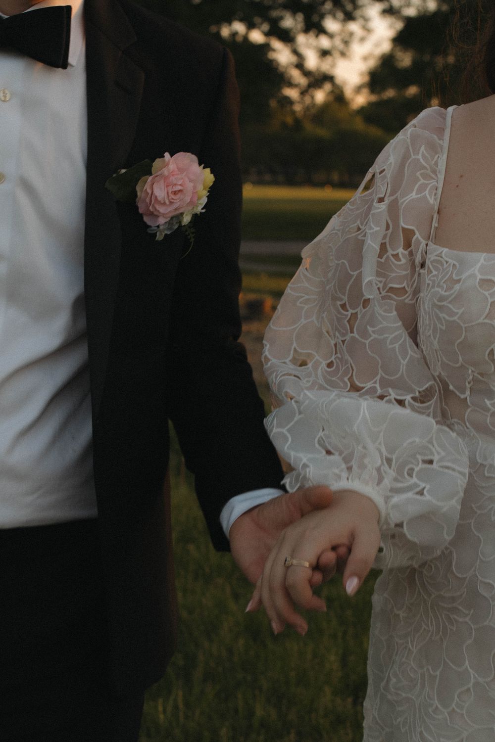Close-up of bride and groom holding hands during sunset wedding ceremony.