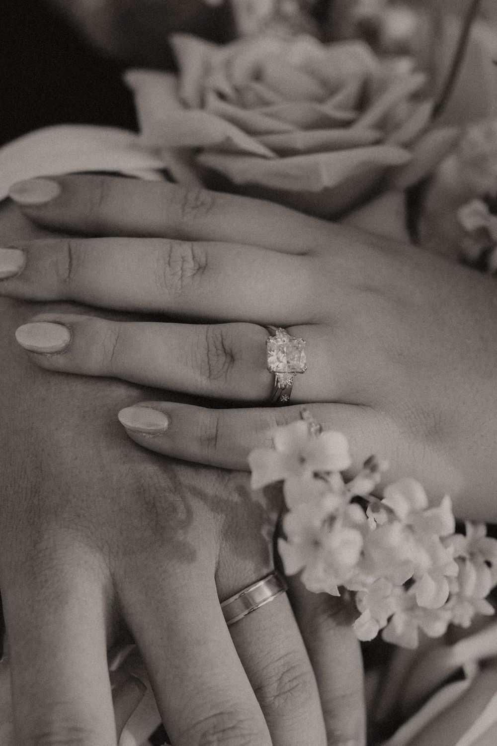 Close-up black and white photos of hands wearing engagement rings with delicate flowers and jewelry.