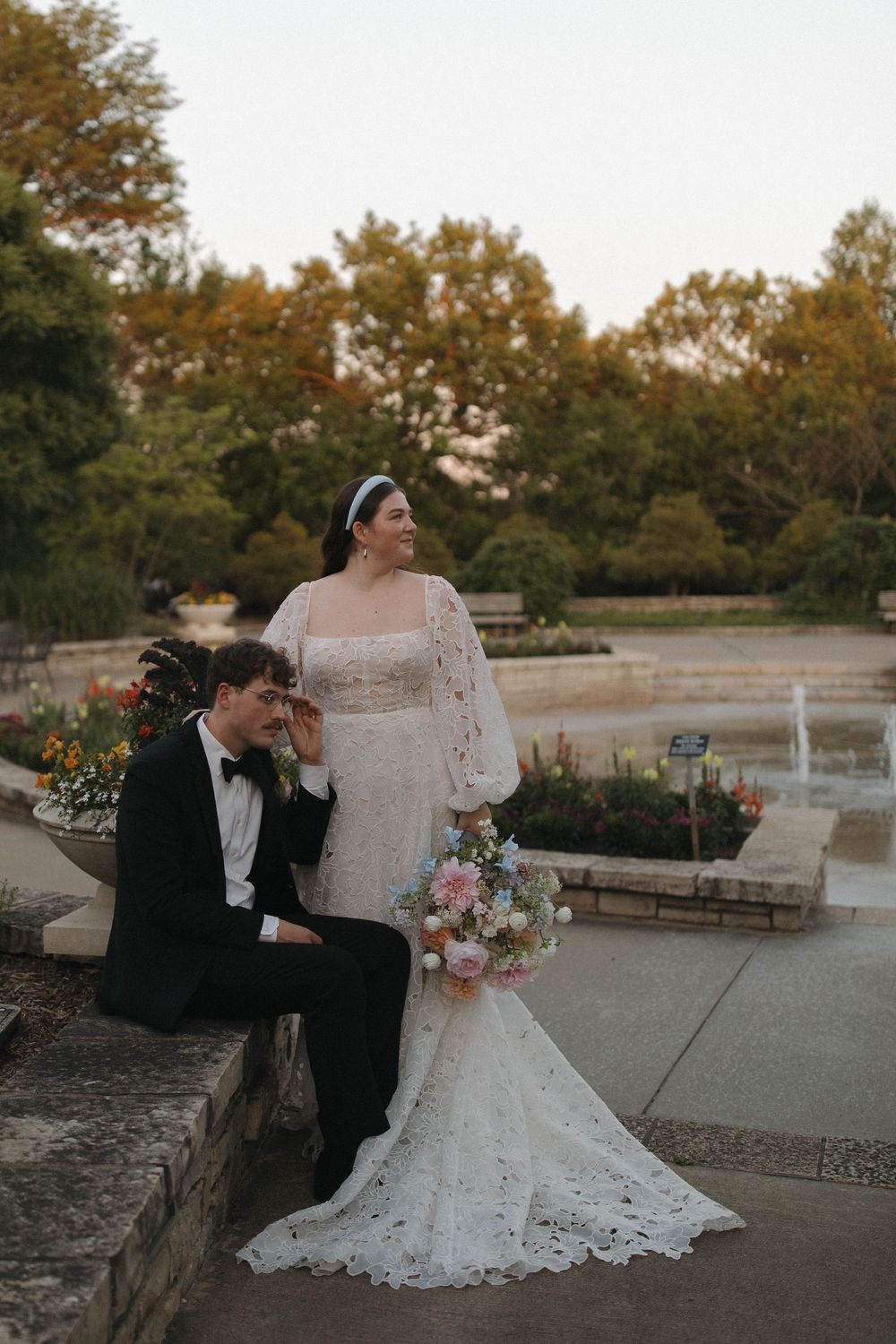 A couple in wedding attire shares playful moments during their sunset photoshoot in an outdoor garden setting.