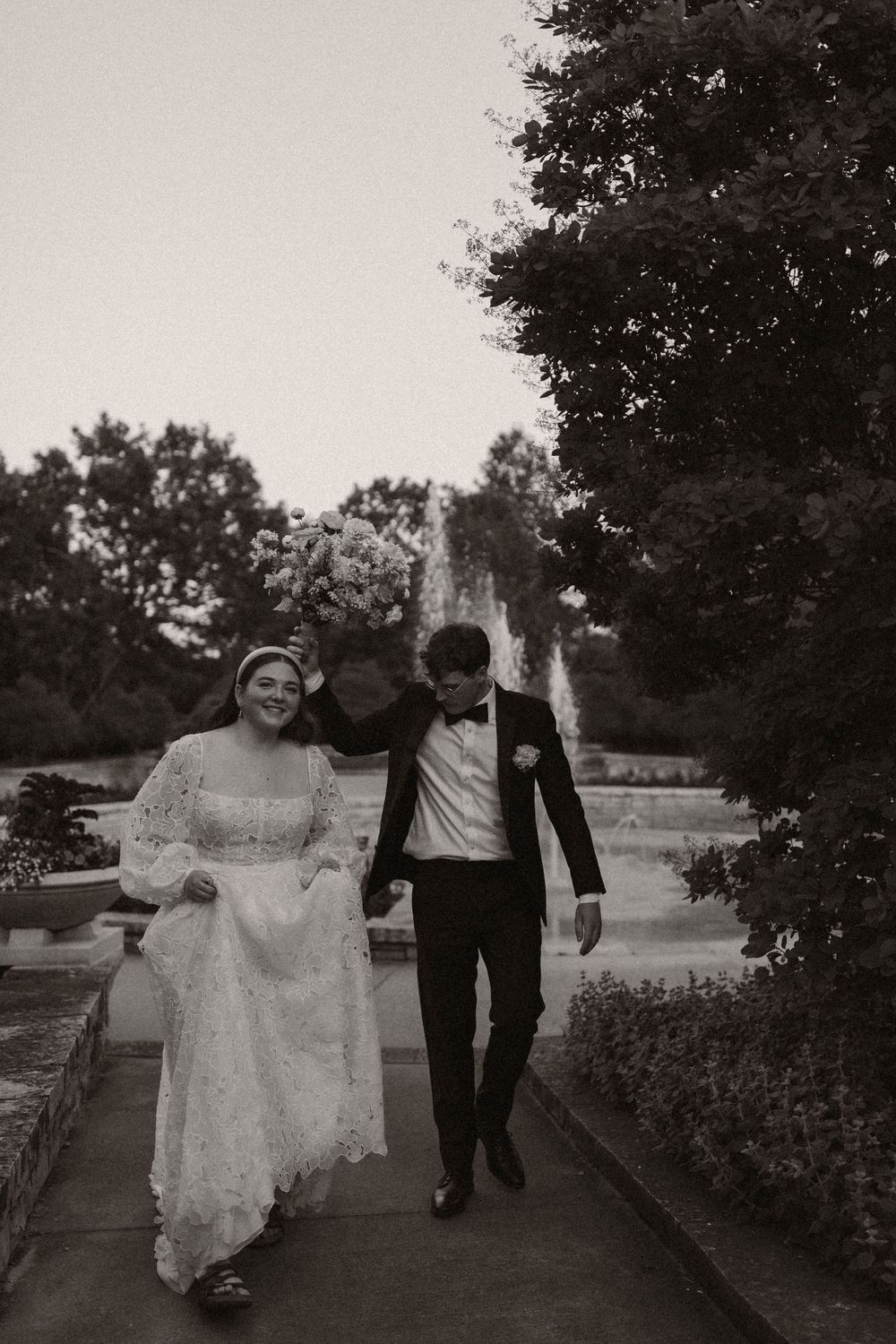 A black and white wedding photo showing a couple walking together along a garden path.