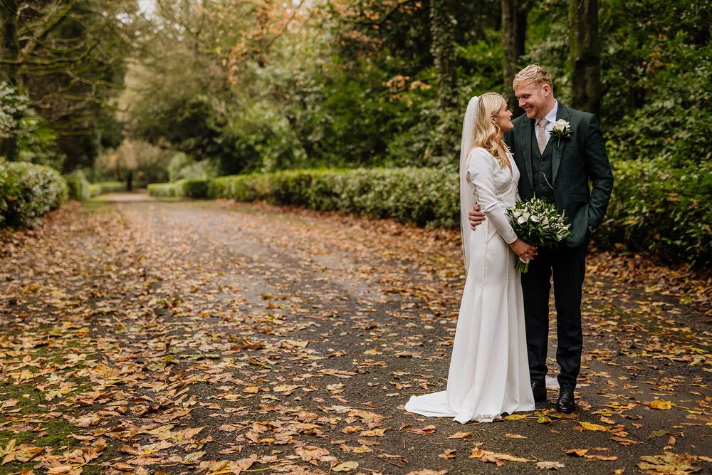 A couple stands on an autumn path covered in fallen leaves during their wedding photoshoot in county Longford.