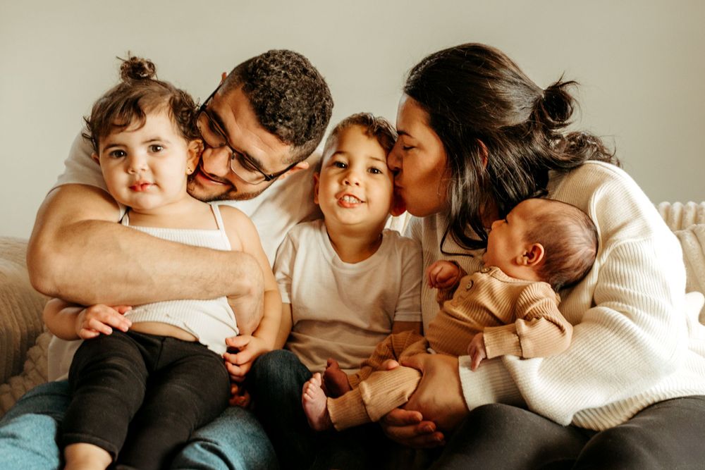 Family sharing affectionate cuddles and kisses together on a couch with their baby.