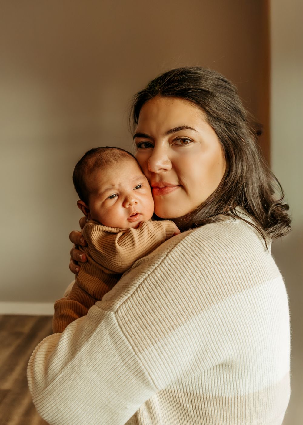 A sweet portrait of parent and baby in matching cream sweaters against a neutral wall.