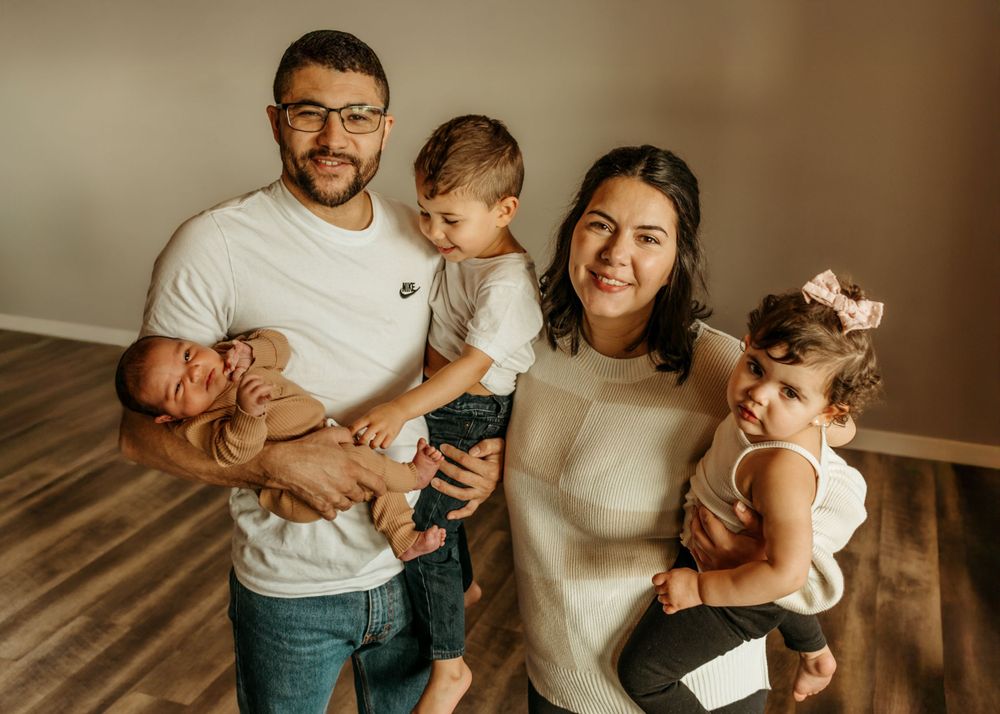 Family of five posing together in a modern home interior with hardwood floors.