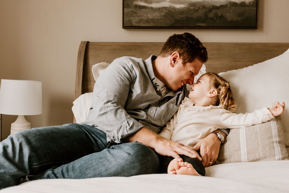 Tender moment shared between adult and baby lying together on a cozy beige couch in a home setting.