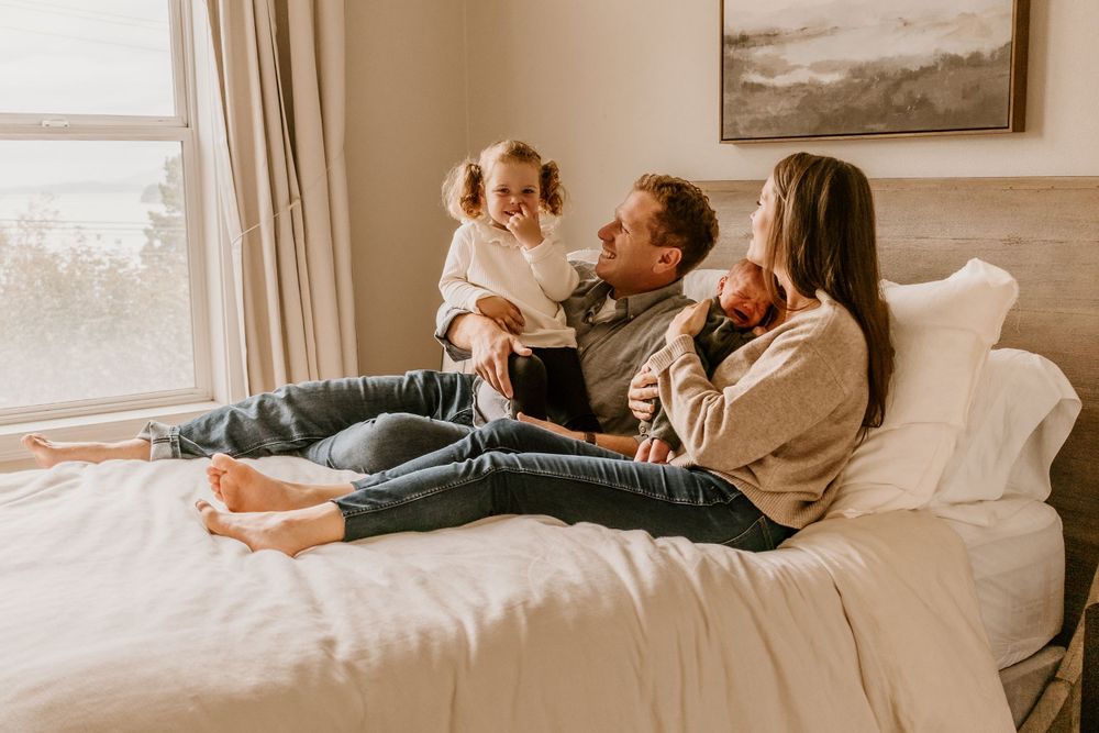 Cozy family moment on white bed near window with natural light streaming in.
