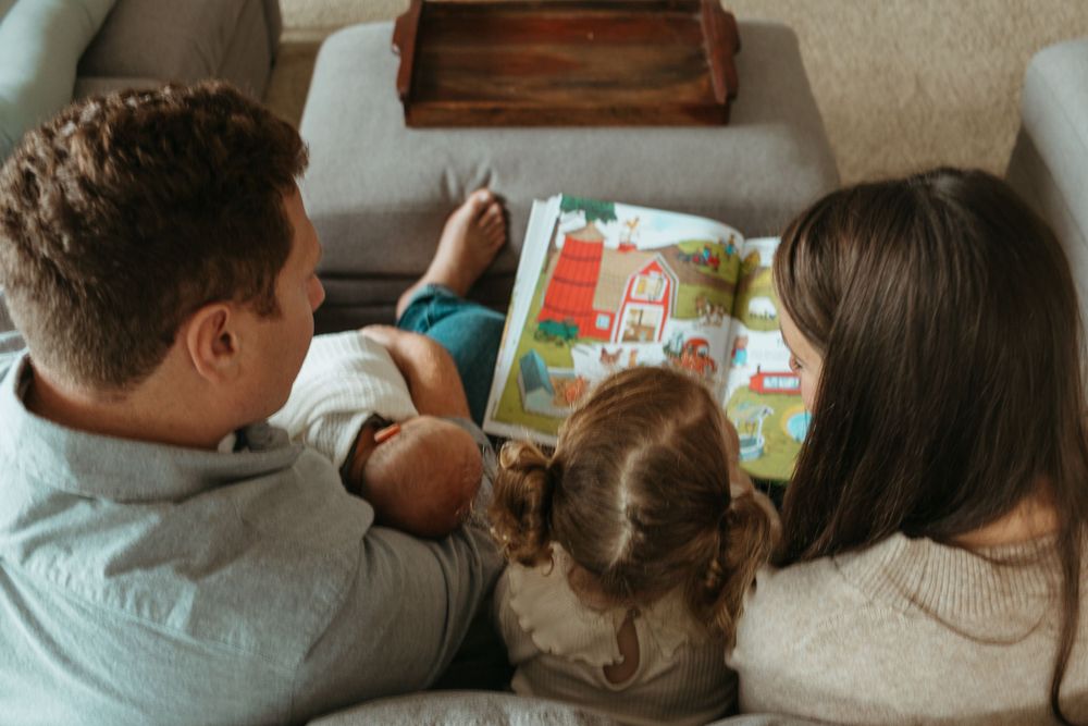 Family enjoying storytime together while reading a children's book on comfortable sofa.